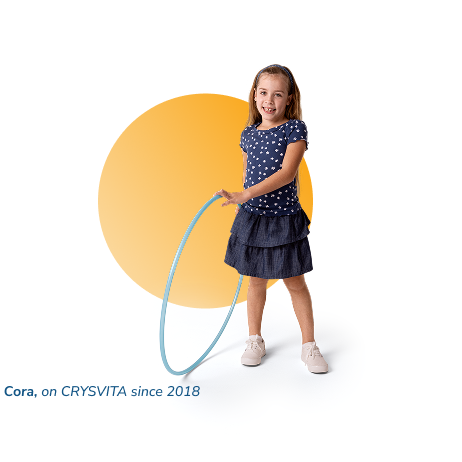 Cora, a child living with XLH, standing and smiling while holding a hula hoop