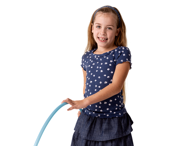 Cora, a child living with XLH, standing and smiling while holding a hula hoop